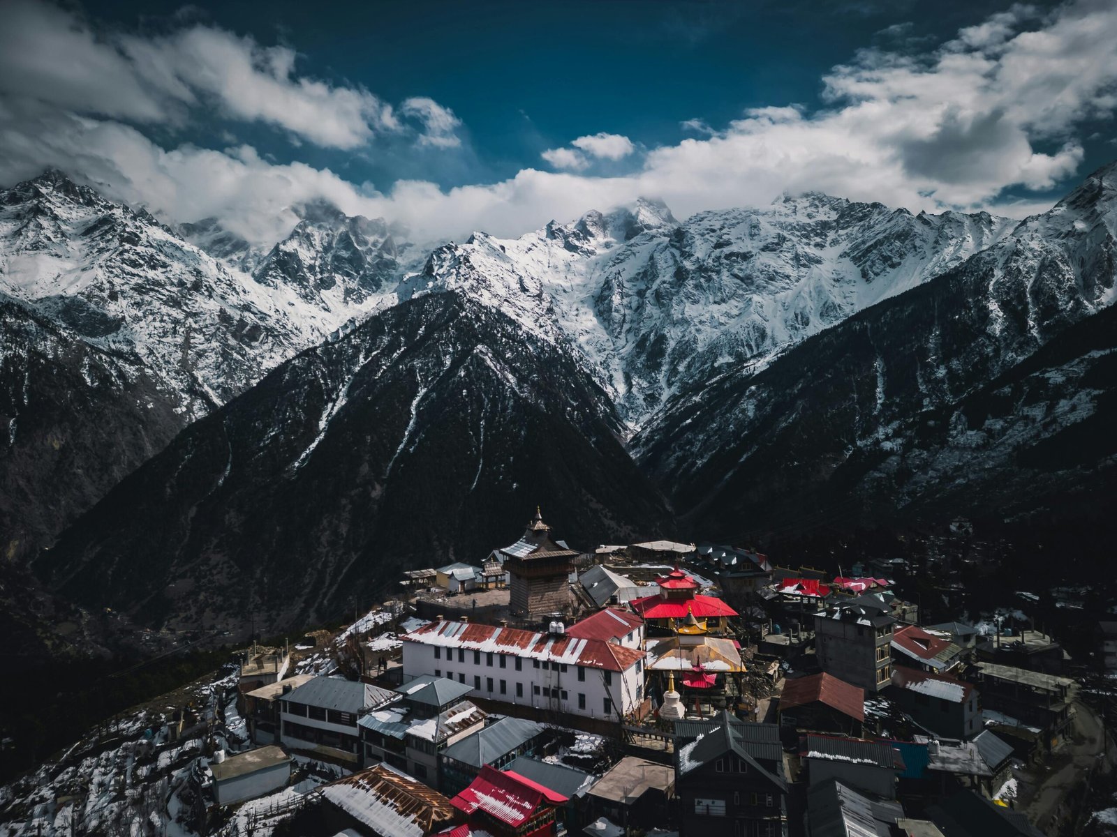 A breathtaking aerial view of a village nestled in the majestic Himachal Himalayas, showcasing snow-capped peaks and vibrant rooftops.