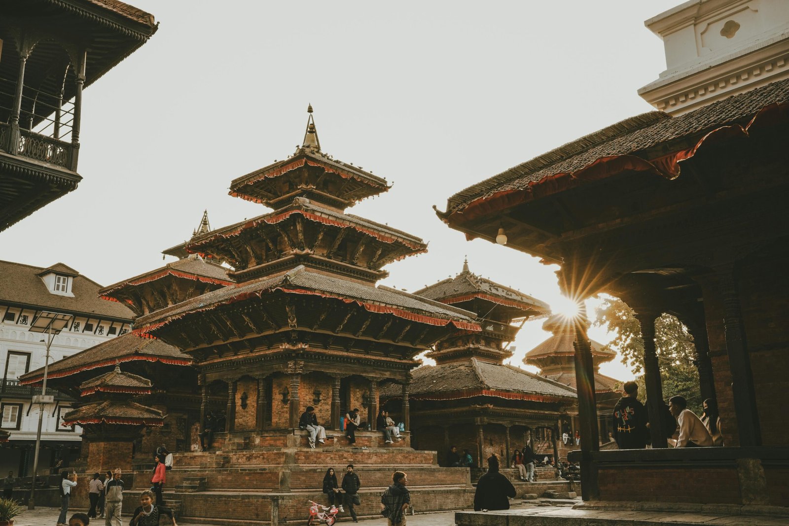 Sunset illuminating ancient temples at Patan Durbar Square, Nepal, with people enjoying the historic ambiance.