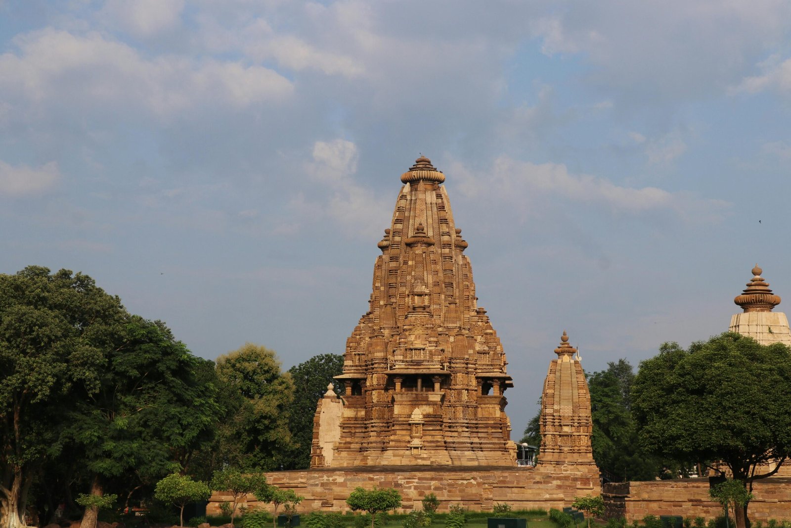Stunning view of the ancient Khajuraho Temple surrounded by lush greenery under a blue sky.